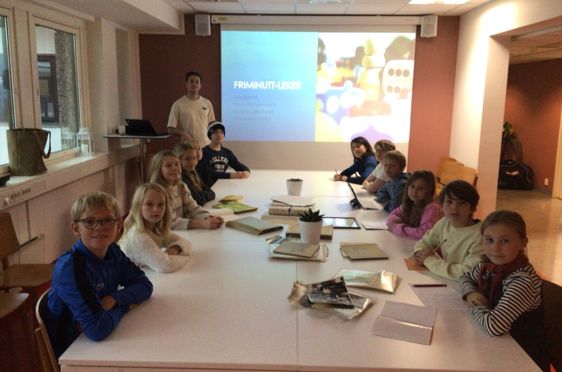 en gruppe barn som sitter ved et bord foran et projektorlerret