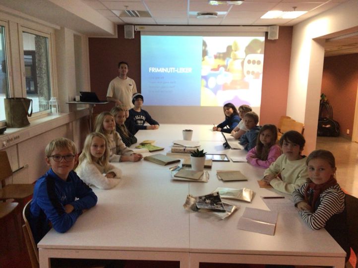 en gruppe barn som sitter ved et bord foran et projektorlerret