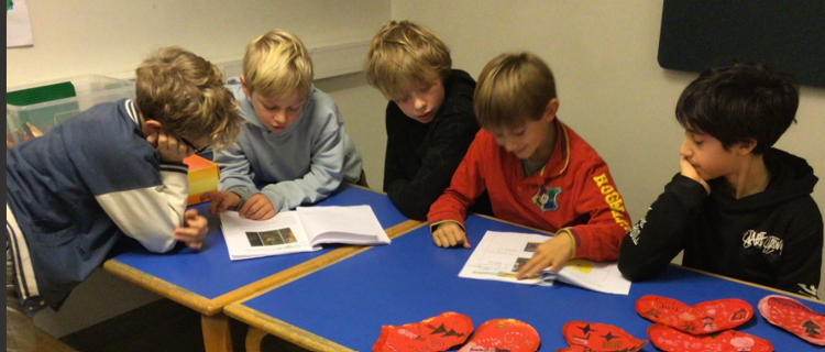 En gruppe barner satt ved et bord og så på papirer
