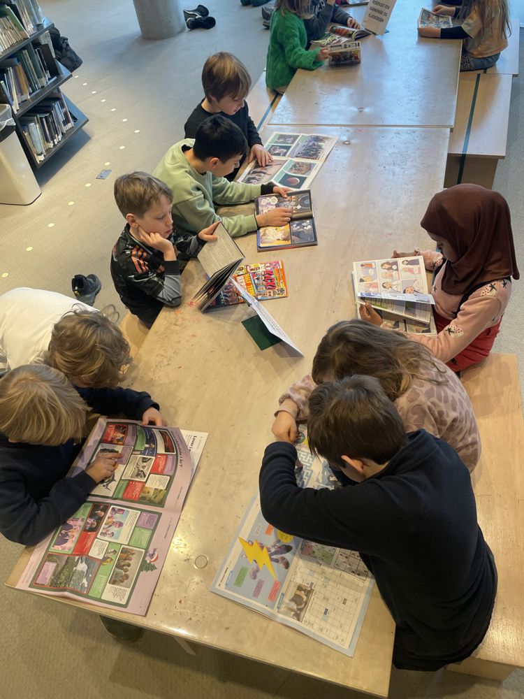 en gruppe barn som sitter ved et bord og ser på en bok