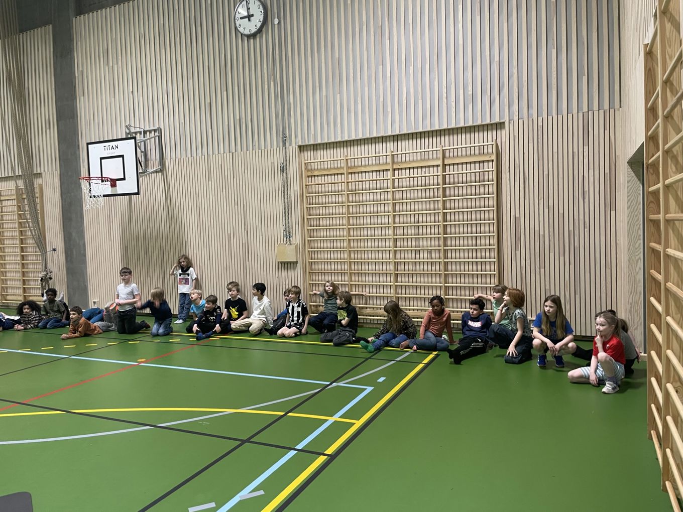 En gruppe mennesker som sitter på gulvet foran en basketballkurv